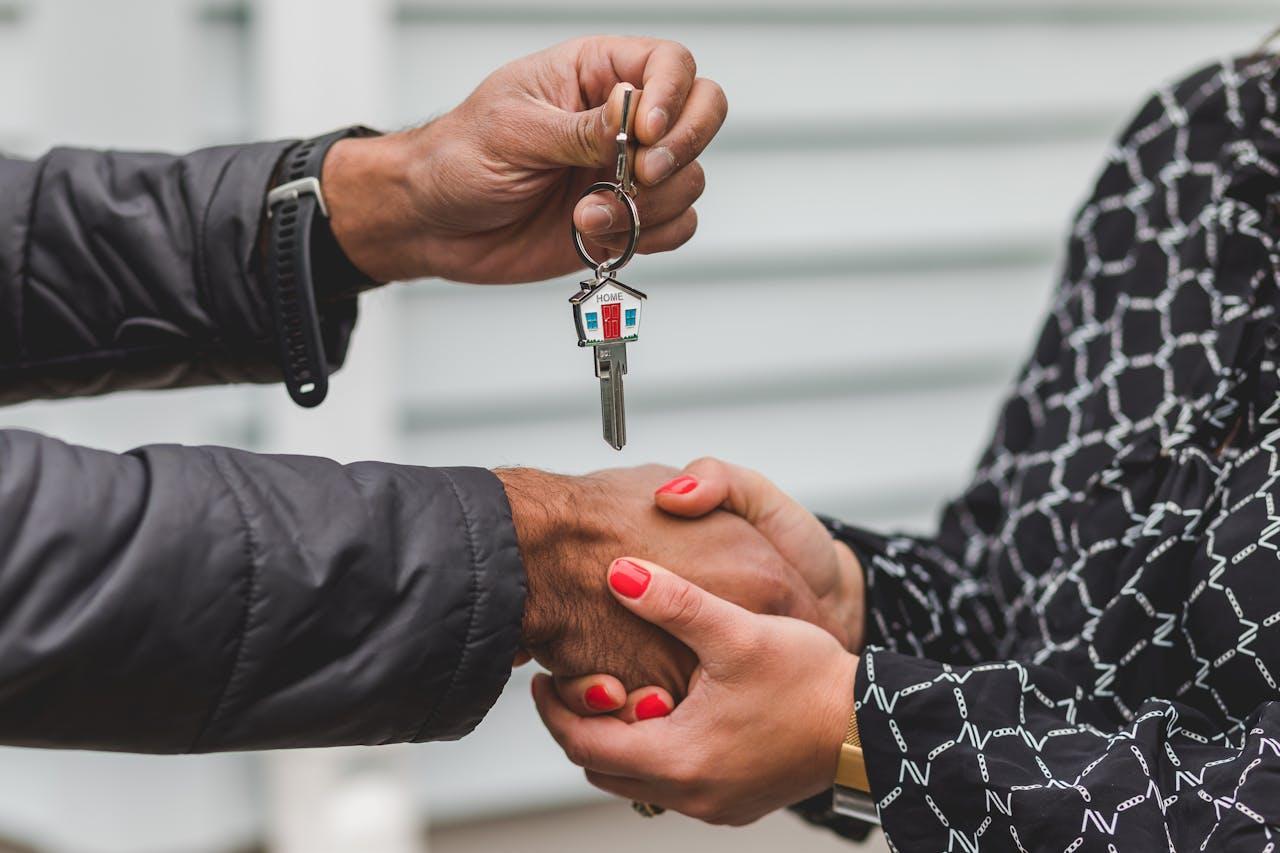 Person holding silver key while shaking lady’s hand