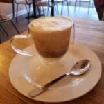 A glass cup of Vietnamese salt coffee with a layer of salted cream foam on top, on a saucer with a spoon