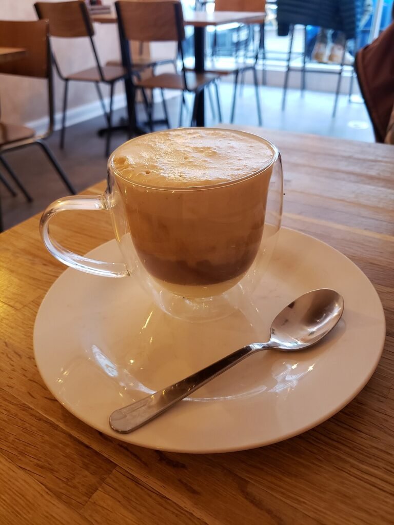 A glass cup of Vietnamese salt coffee with a layer of salted cream foam on top, on a saucer with a spoon