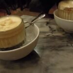 Two glasses of Vietnamese egg coffee with whipped yolk foam, each set in a bowl of hot water