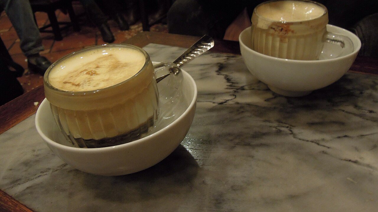 Two glasses of Vietnamese egg coffee with whipped yolk foam, each set in a bowl of hot water